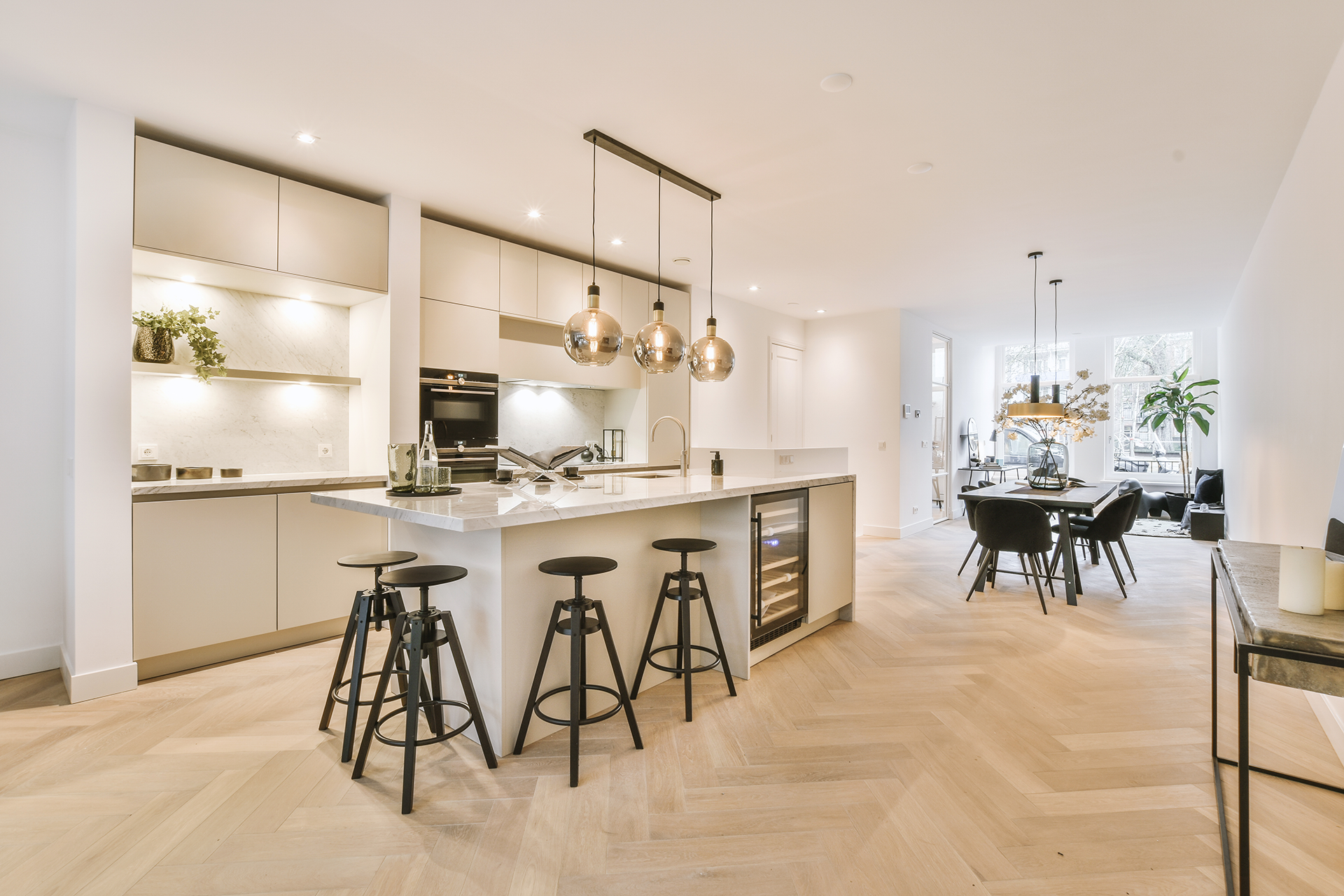 Minimalist modern kitchen open concept into living space. Neutral frameless cabinets. Under cabinet lighting and island with seating.